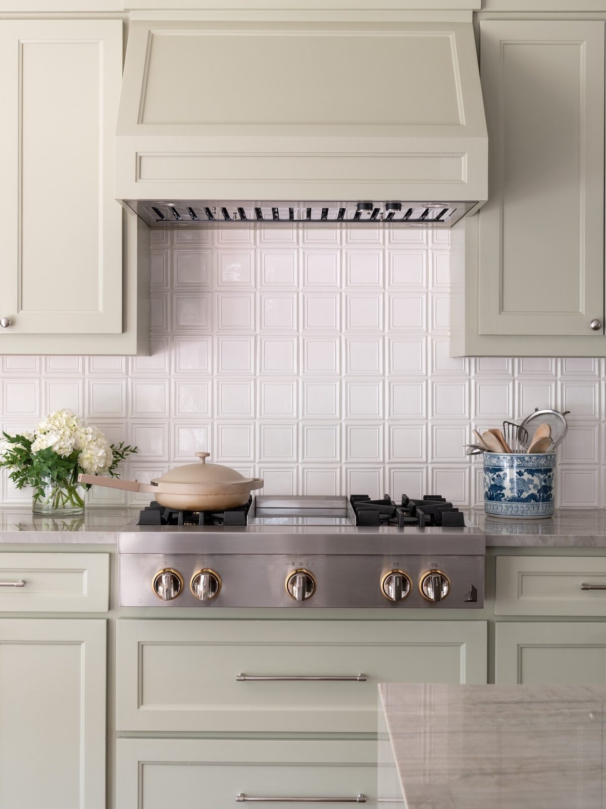 Photo of stove top in kitchen with sage green drawers and cabinets